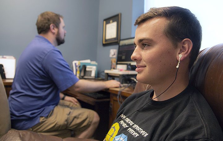 A Man sitting in a chair with sensors on his ears and another man on a computer.