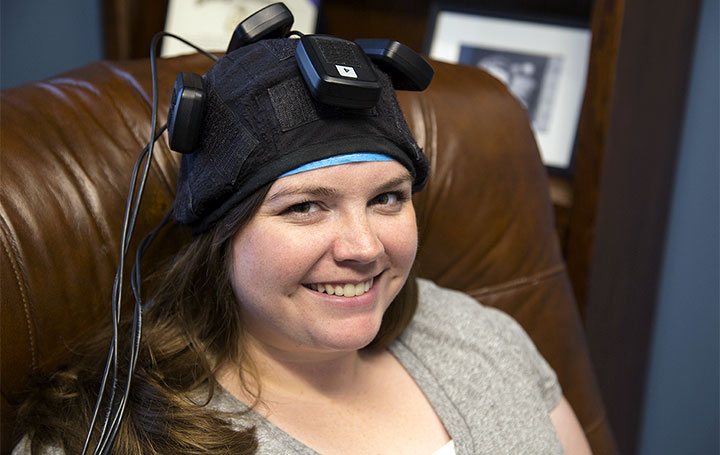 A Man sitting in a chair with sensors on his ears and another man on a computer.